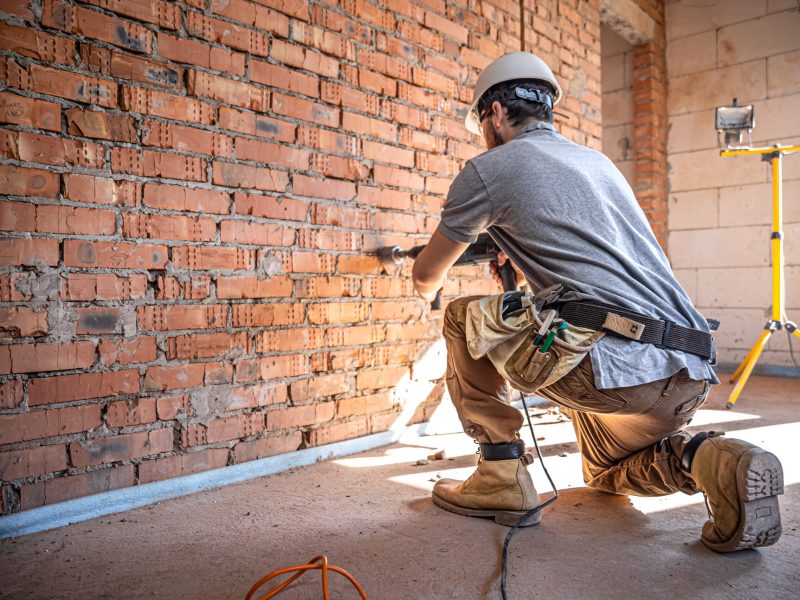 Handyman at a construction site in the process of drilling a wall with a perforator.